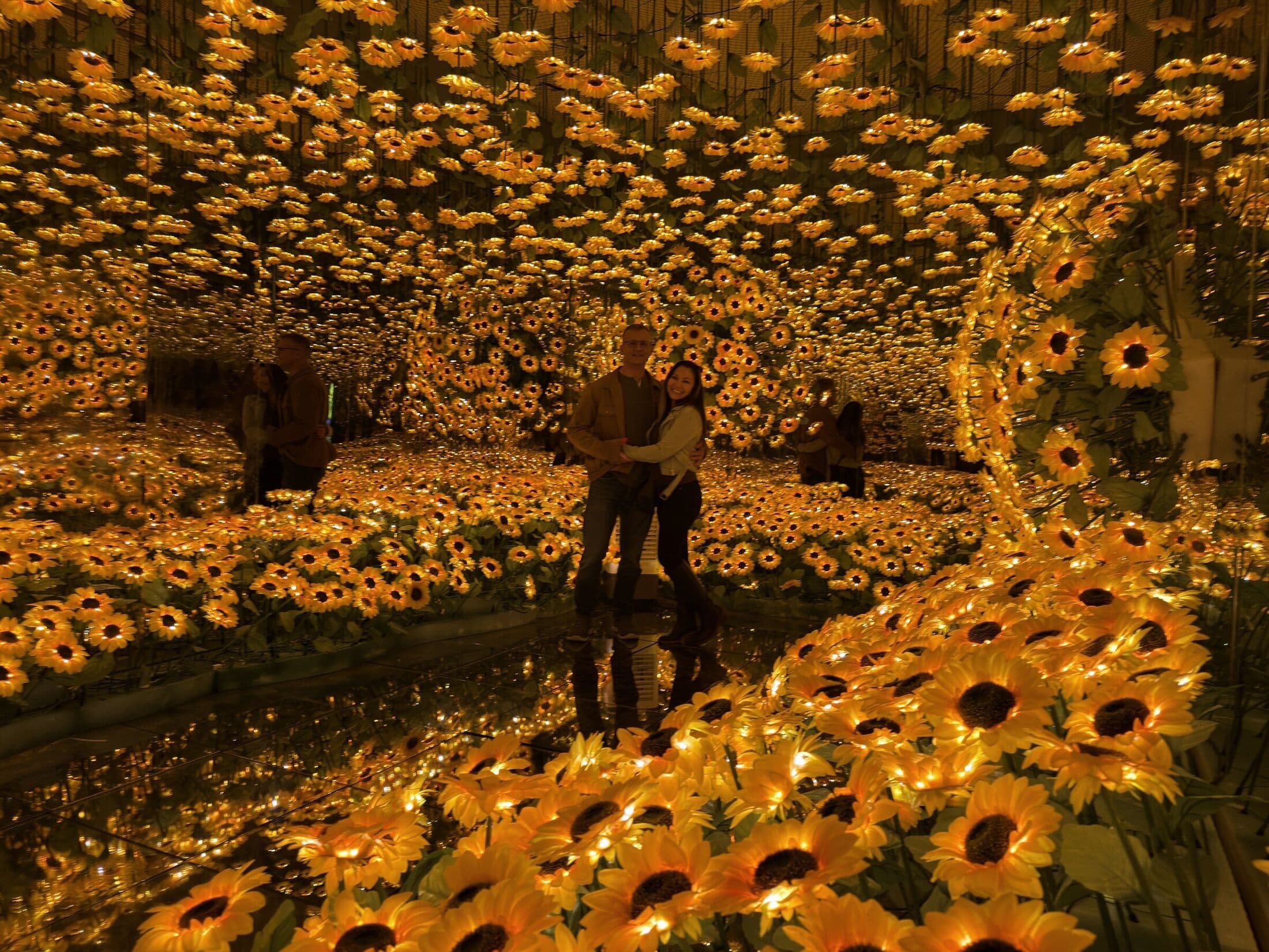 Two people standing together inside the Imaginarium sunflower mirror room.