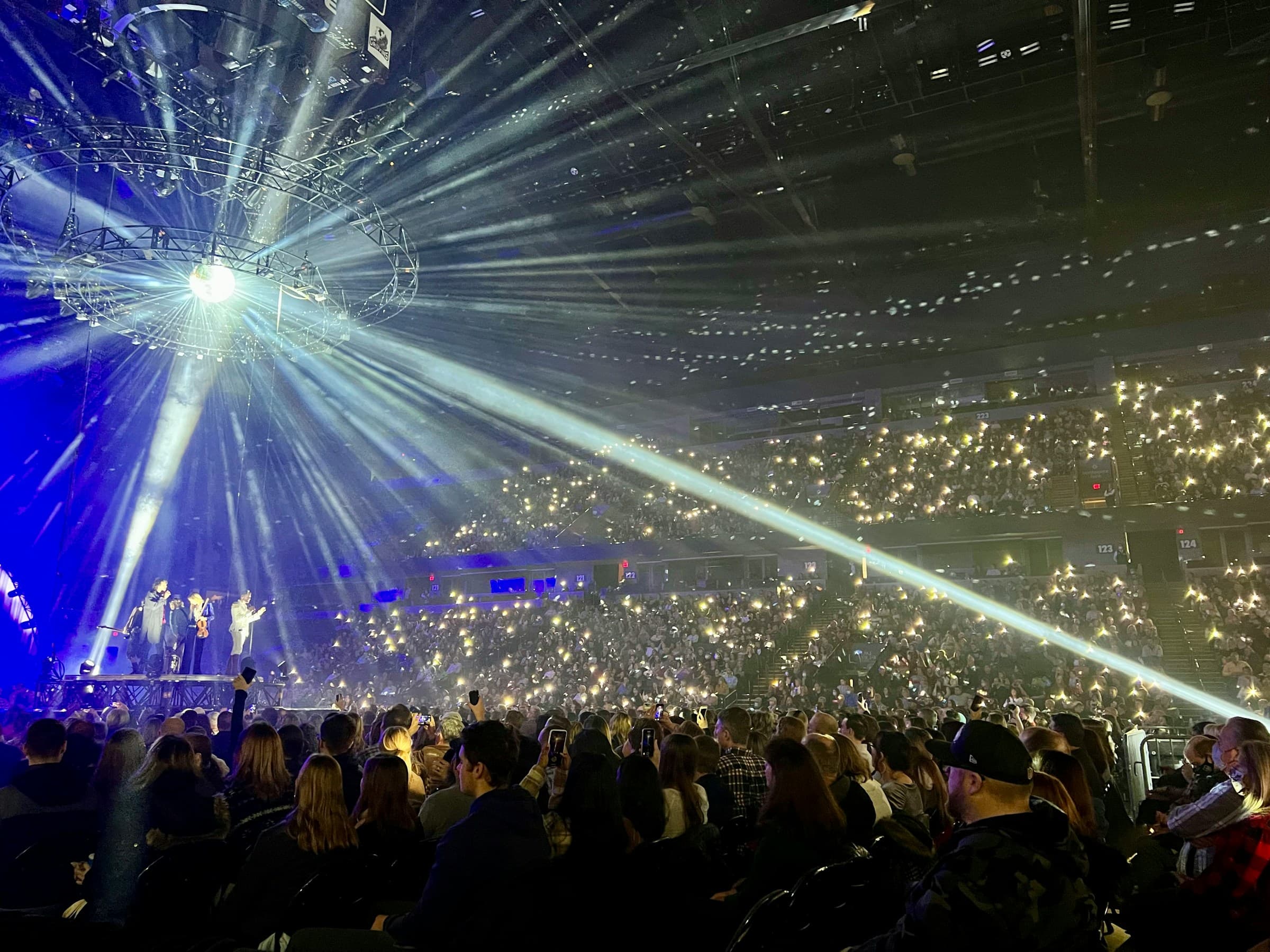 A concert crowd with hands raised beneath bright stage lights.